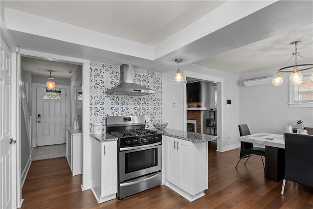 kitchen with stainless steel gas range oven, wall chimney range hood, hanging light fixtures, dark hardwood / wood-style floors, and white cabinetry