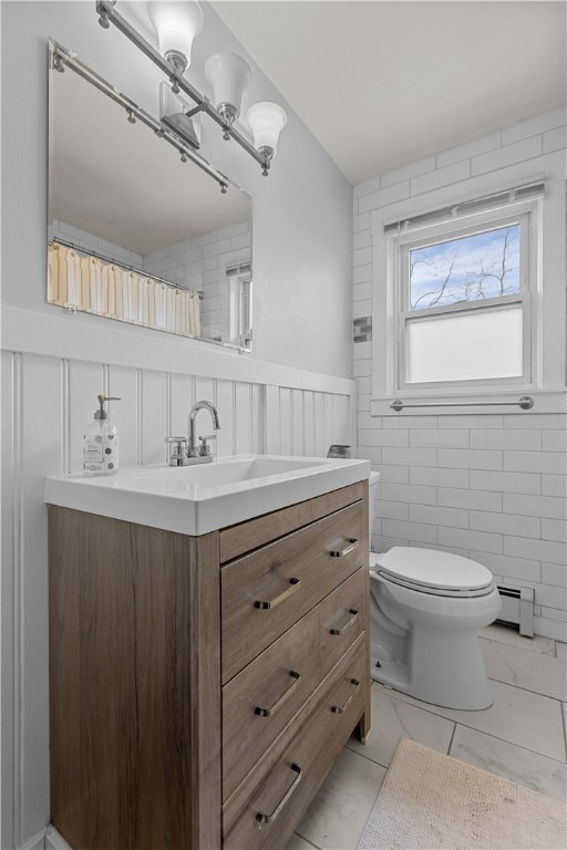 bathroom featuring toilet, vanity, tile walls, and a baseboard heating unit