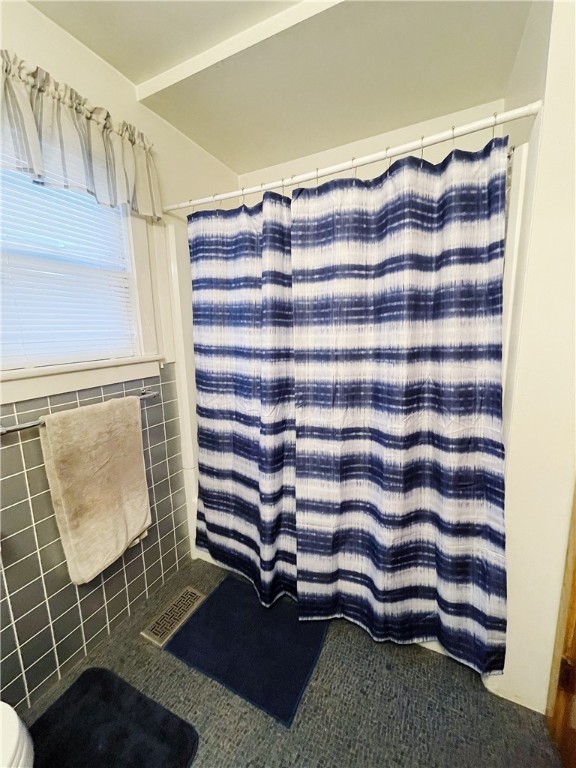 bathroom featuring walk in shower, toilet, and tile walls