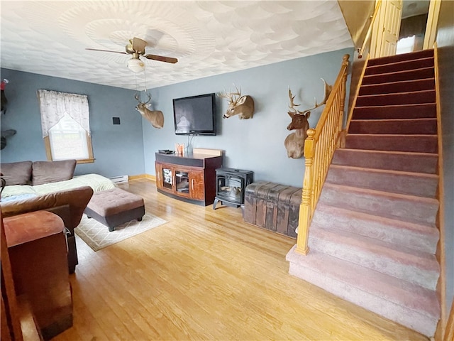 living room featuring hardwood / wood-style floors, ceiling fan, a wood stove, and baseboard heating