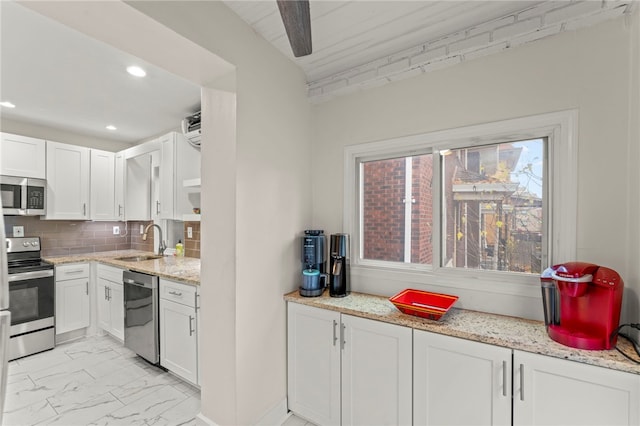 kitchen featuring sink, light stone counters, appliances with stainless steel finishes, white cabinets, and backsplash