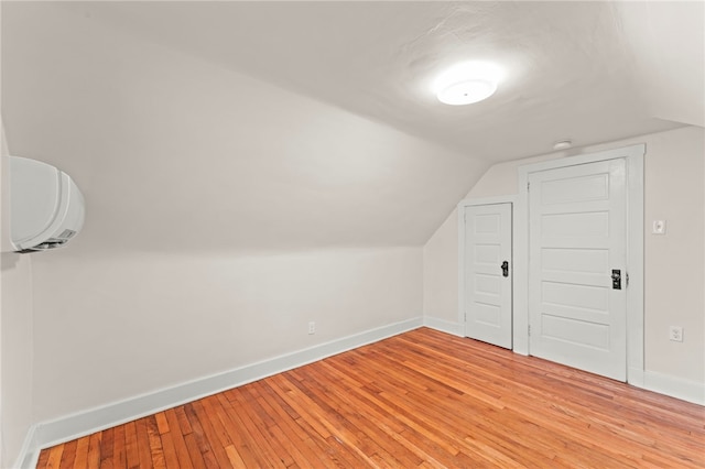 additional living space featuring vaulted ceiling, a wall unit AC, and light wood-type flooring