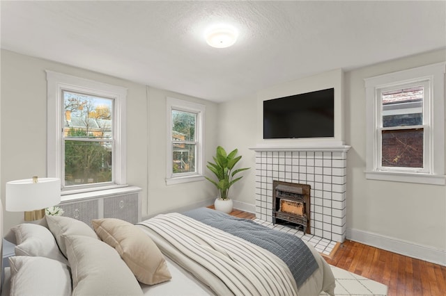 bedroom with hardwood / wood-style floors, a fireplace, radiator, and a textured ceiling