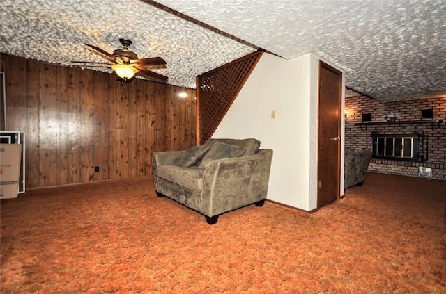 living area with carpet flooring, ceiling fan, wood walls, a textured ceiling, and a fireplace