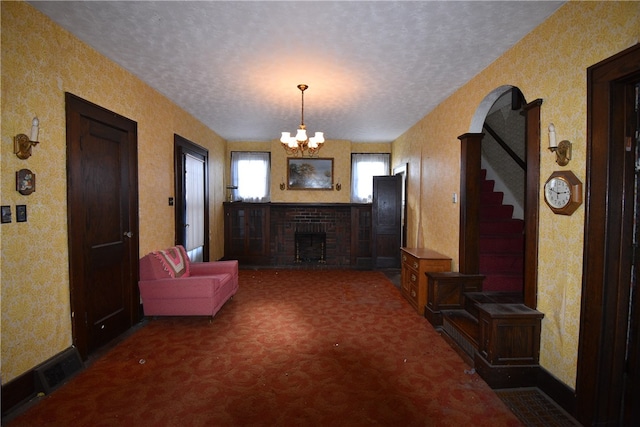 living room with dark colored carpet, a textured ceiling, an inviting chandelier, and a brick fireplace