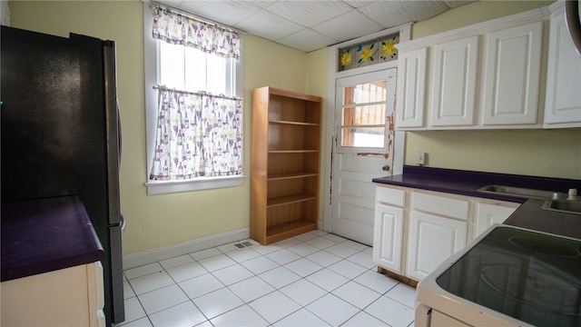 kitchen featuring black refrigerator, a drop ceiling, range, white cabinetry, and light tile patterned flooring