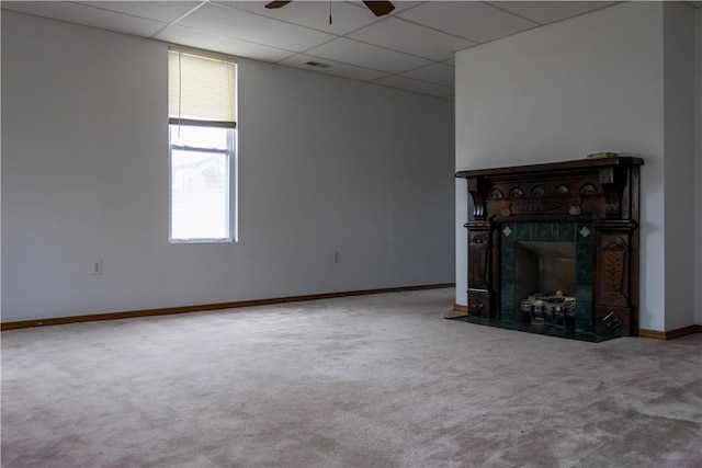 unfurnished living room with a paneled ceiling, carpet flooring, ceiling fan, and a tiled fireplace