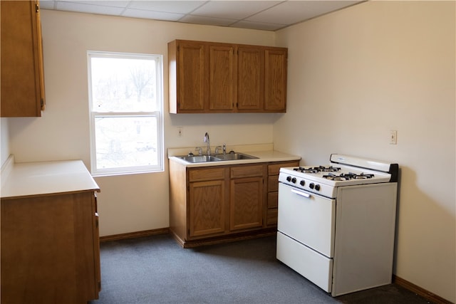 kitchen featuring a paneled ceiling, dark colored carpet, white gas stove, and sink