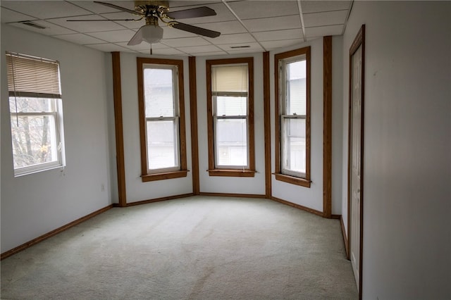 spare room featuring a drop ceiling, ceiling fan, light carpet, and a wealth of natural light