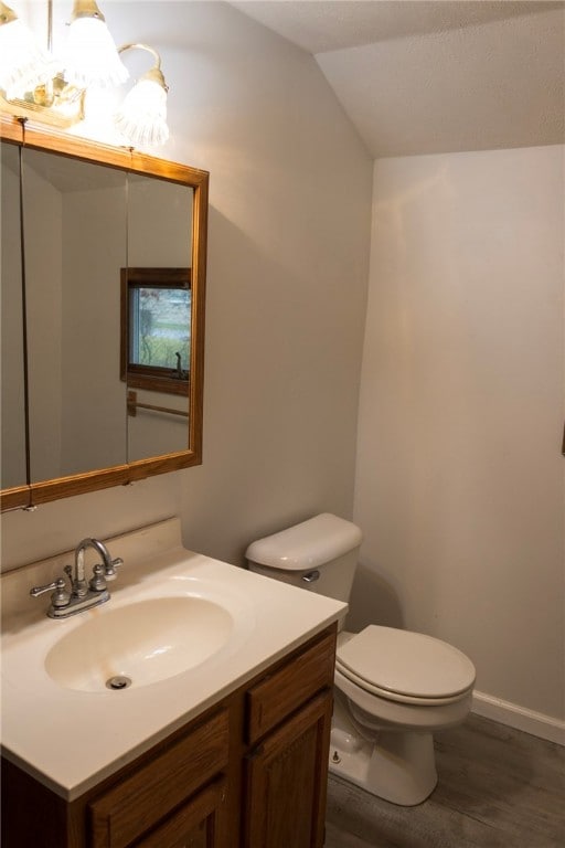 bathroom with toilet, vanity, vaulted ceiling, and hardwood / wood-style flooring