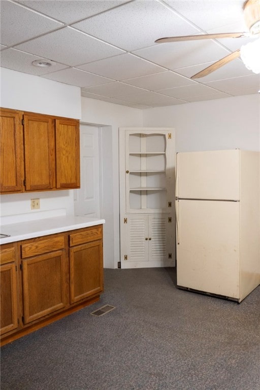 kitchen with ceiling fan, white refrigerator, a drop ceiling, and dark carpet