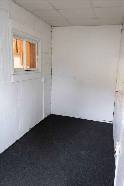 carpeted empty room with a paneled ceiling and wood walls