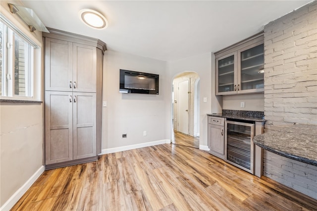 kitchen with gray cabinets, light hardwood / wood-style floors, beverage cooler, and dark stone counters