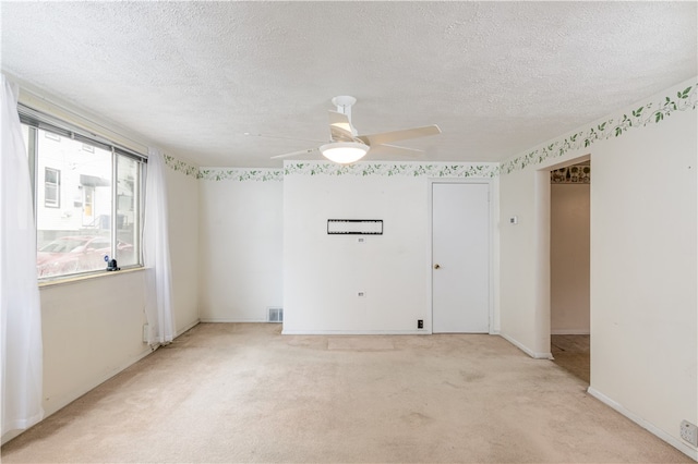 empty room featuring a textured ceiling, light colored carpet, and ceiling fan