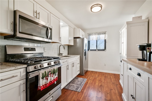 kitchen featuring light stone countertops, stainless steel appliances, sink, white cabinets, and light hardwood / wood-style floors