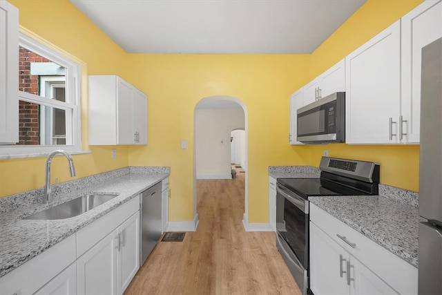 kitchen with white cabinets, sink, light hardwood / wood-style floors, light stone counters, and stainless steel appliances