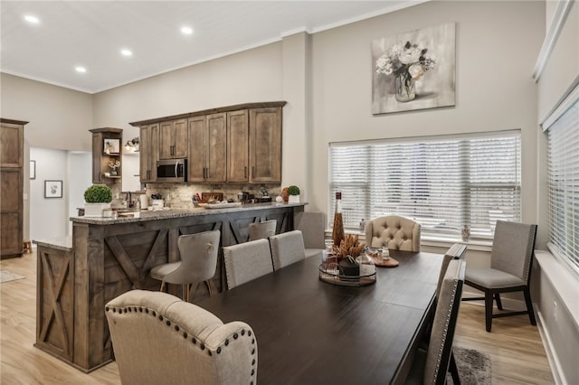 dining space with a towering ceiling, ornamental molding, and light wood-type flooring