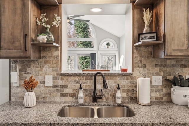 kitchen featuring backsplash, light stone counters, vaulted ceiling, and sink