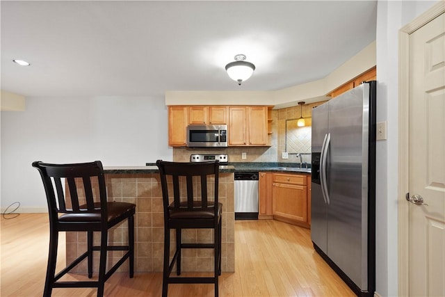 kitchen featuring sink, a kitchen breakfast bar, backsplash, light hardwood / wood-style floors, and appliances with stainless steel finishes