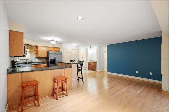 kitchen featuring light hardwood / wood-style flooring, stainless steel fridge, tasteful backsplash, kitchen peninsula, and a breakfast bar area