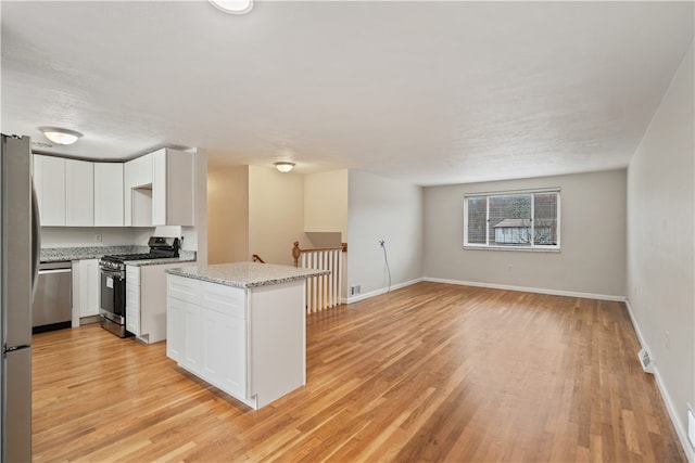 kitchen featuring light stone countertops, white cabinetry, kitchen peninsula, appliances with stainless steel finishes, and light wood-type flooring