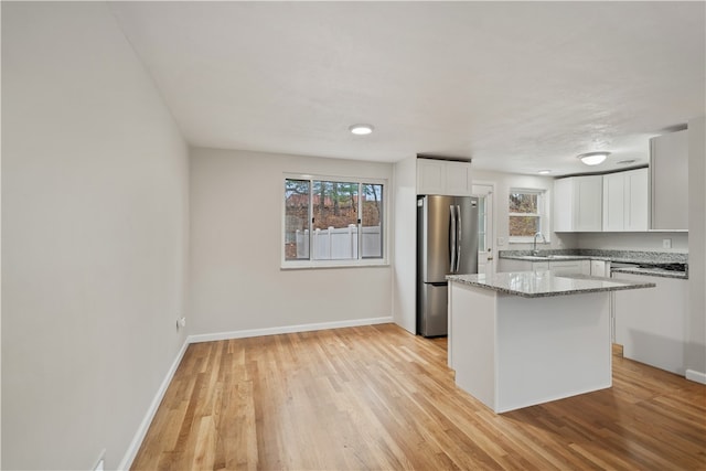 kitchen with white cabinets, light stone countertops, light wood-type flooring, a kitchen island, and stainless steel refrigerator