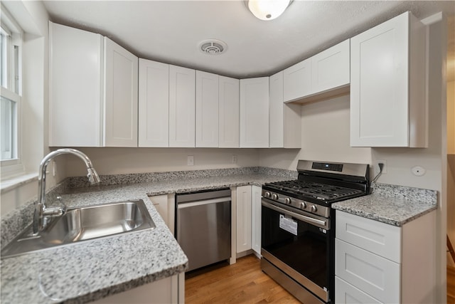 kitchen with light stone countertops, sink, stainless steel appliances, light hardwood / wood-style floors, and white cabinets