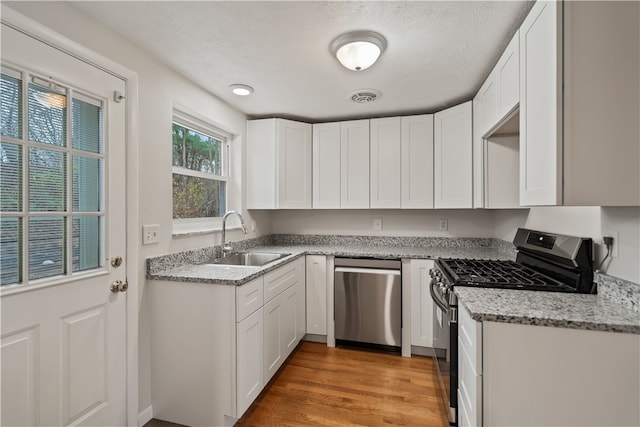 kitchen with white cabinets, light wood-type flooring, stainless steel appliances, and sink