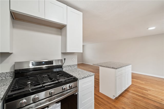 kitchen featuring white cabinets, light stone countertops, light hardwood / wood-style flooring, and gas range