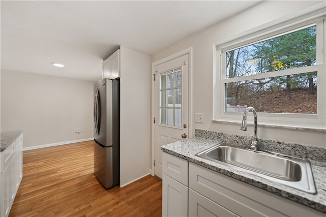 kitchen featuring sink, light hardwood / wood-style flooring, light stone countertops, white cabinetry, and stainless steel refrigerator