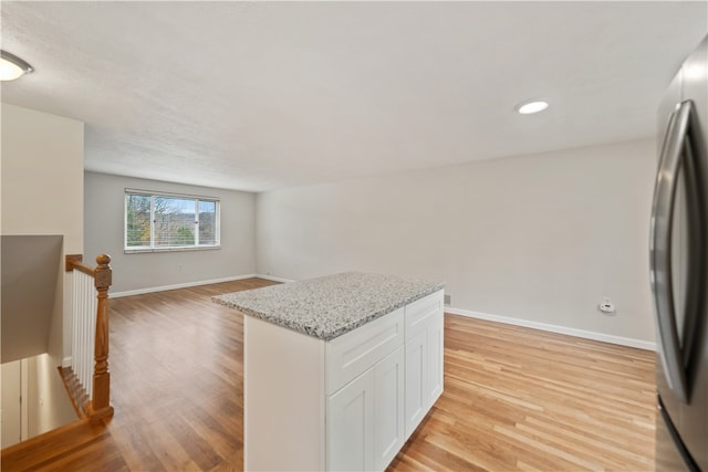 kitchen featuring stainless steel refrigerator, white cabinets, light stone counters, a kitchen island, and light wood-type flooring