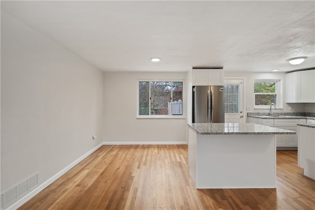 kitchen with white cabinets, light stone countertops, stainless steel refrigerator, and light hardwood / wood-style flooring