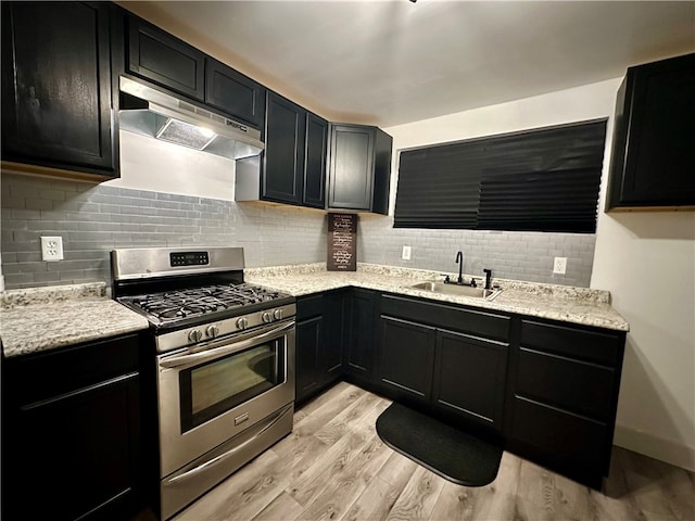 kitchen featuring sink, decorative backsplash, light stone counters, stainless steel gas range, and light hardwood / wood-style flooring