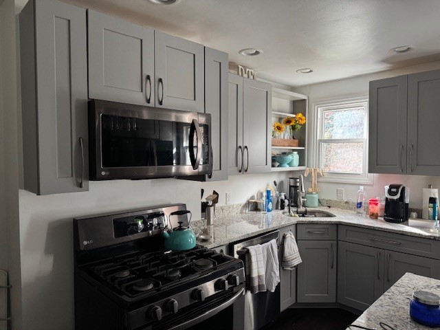 kitchen with light stone counters, gray cabinets, sink, and stainless steel appliances