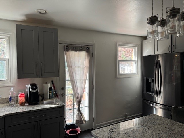 kitchen with gray cabinetry, light stone counters, plenty of natural light, and stainless steel refrigerator with ice dispenser