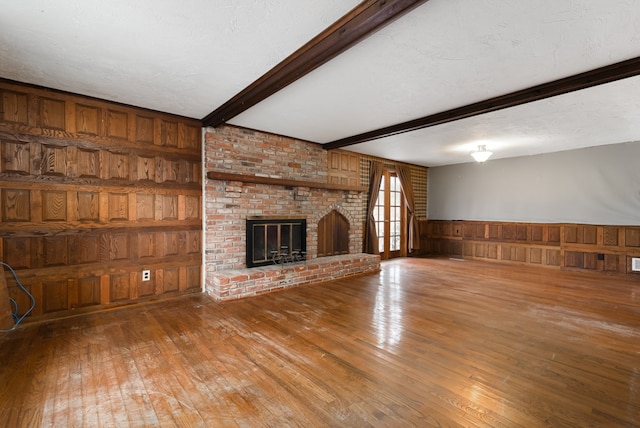 unfurnished living room with beam ceiling, a brick fireplace, wood walls, hardwood / wood-style floors, and a textured ceiling