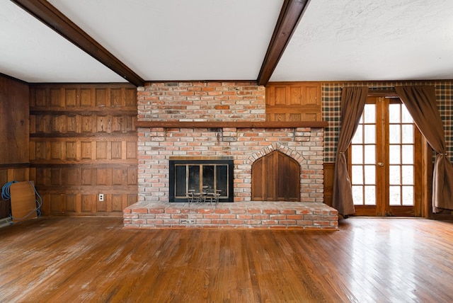 unfurnished living room featuring wood walls, french doors, hardwood / wood-style flooring, a fireplace, and beamed ceiling