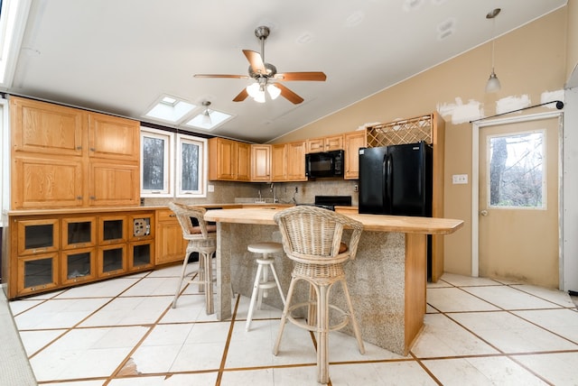 kitchen with decorative backsplash, a kitchen breakfast bar, lofted ceiling with skylight, black appliances, and decorative light fixtures