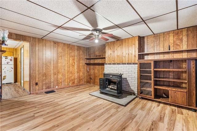 unfurnished living room with a paneled ceiling, ceiling fan, a wood stove, and hardwood / wood-style flooring