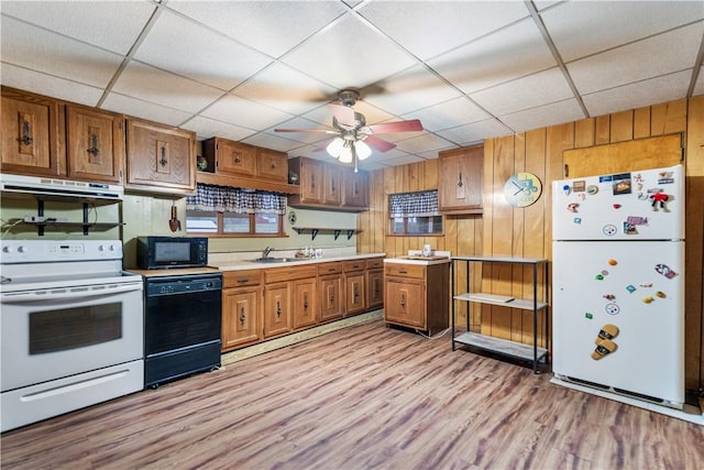 kitchen with light wood-type flooring, ceiling fan, wooden walls, sink, and black appliances