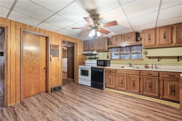 kitchen with ceiling fan, wooden walls, sink, black appliances, and light hardwood / wood-style floors