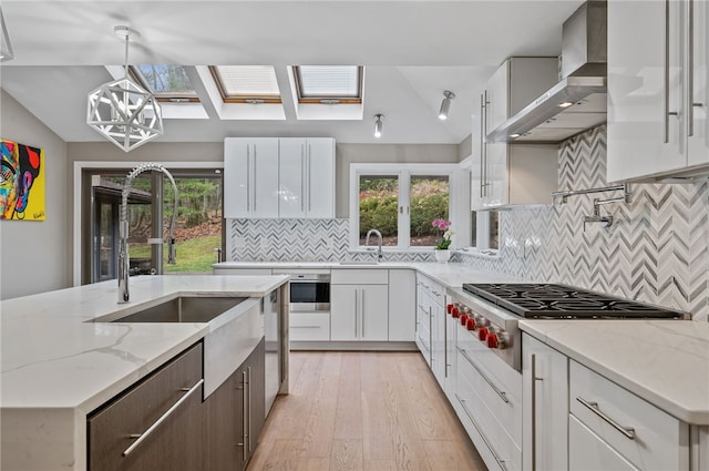 kitchen featuring a skylight, white cabinetry, wall chimney exhaust hood, and light hardwood / wood-style flooring