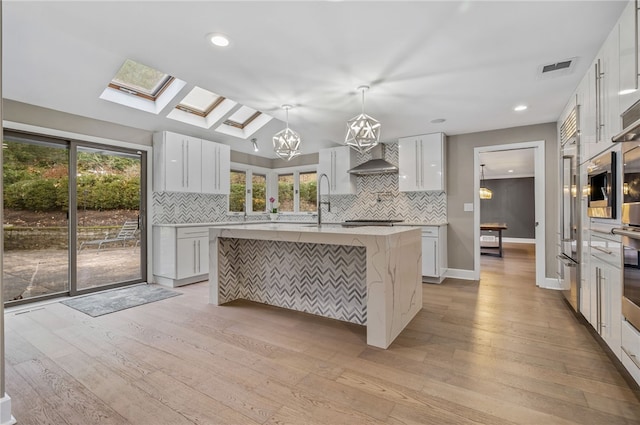 kitchen with white cabinets, pendant lighting, light hardwood / wood-style floors, and a center island with sink