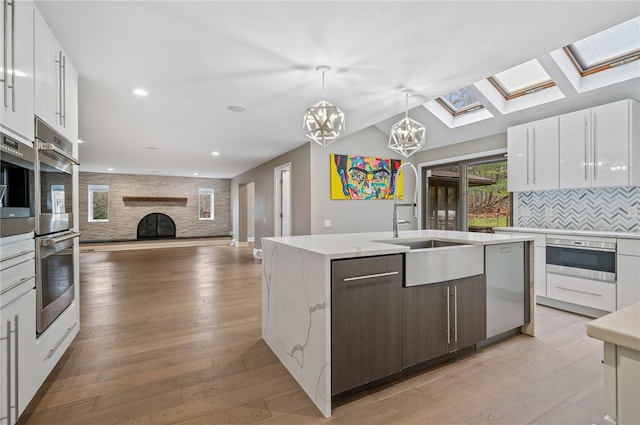 kitchen featuring a kitchen island with sink, dark brown cabinets, white cabinets, and light wood-type flooring