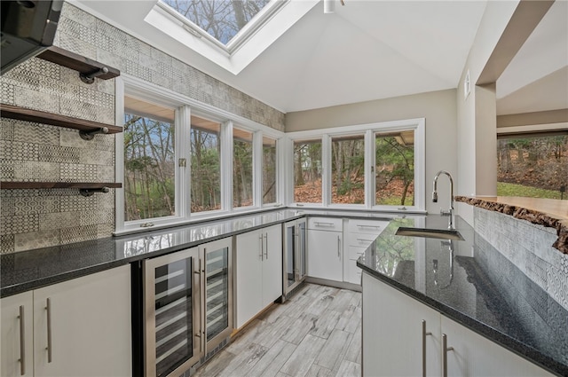 kitchen with decorative backsplash, vaulted ceiling with skylight, sink, white cabinets, and wine cooler