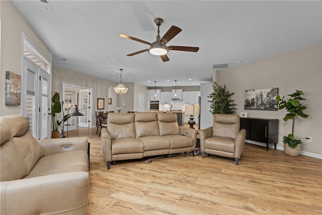 living room with ceiling fan with notable chandelier and light hardwood / wood-style floors