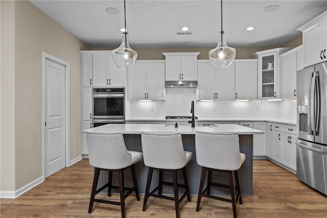 kitchen with appliances with stainless steel finishes, a center island with sink, white cabinetry, and pendant lighting