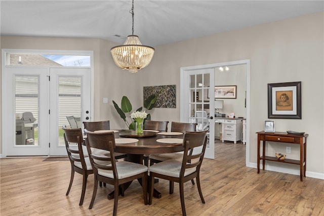 dining area with a notable chandelier, light wood-type flooring, and french doors