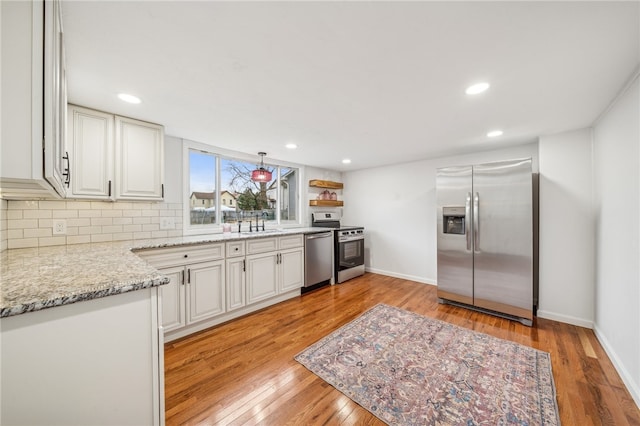 kitchen with white cabinets, backsplash, light wood-type flooring, and stainless steel appliances