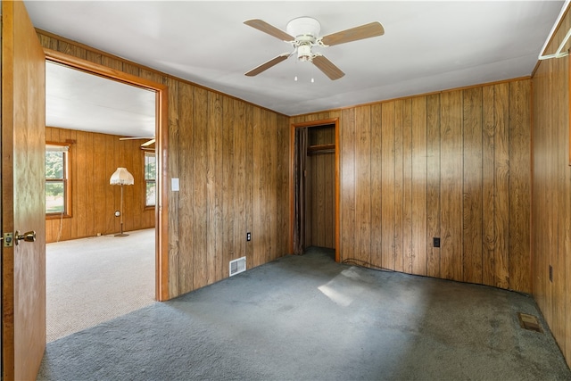 spare room with wooden walls, ceiling fan, and dark carpet